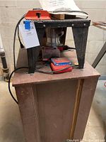 Front view of the router/sabre saw table with orange safety accessory, instruction manual, mounted on wooden cart.