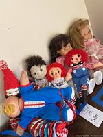 Photo showing seven assorted dolls including Raggedy Ann and Andy, Cabbage Patch style dolls, and a baby doll with large yellow pacifier.