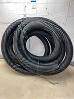 Coiled large black plastic corrugated drainage tubing tied with green and black cords, showing overall lot contents.
