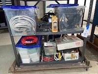 Shelf with multiple plastic bins containing various electronic cables including white coaxial cables, black and red wires, and connectors. Also visible reel of red cable.