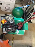 Overall view of emergency car kit with Black & Decker vacuum, tire repair kit, jumper cables, scraper, and toolset in a basement setting.