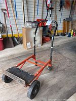 Full view of hand truck dolly with orange frame and black handle in warehouse setting.