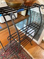 Front and side view of the black metal plant stand showing three wire shelves and decorative curved sides.