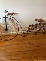 Wide shot of both the vintage penny-farthing bicycle metal wall decor and the autumn leaves metal wall hanging on the floor against a white wall