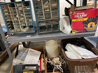 Shelf with various items including trash bags, rope, a plastic basket of bags, and workshop storage bins with assorted hardware.
