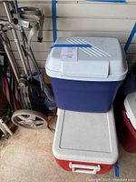 Photo showing stacked coolers with a small blue Rubbermaid cooler on top of a larger red Coleman chest cooler, located in a garage.