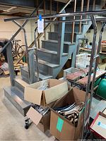 Full view of double metal clothing rack with wheels near staircase and three boxes of assorted hangers on floor.