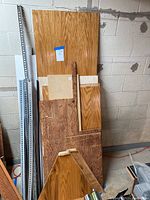 Large and various smaller plywood sheets leaning against a wall with several metal corner strips on the left.