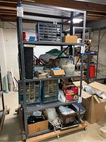 Front view of the two mounted metal shelving units loaded with various small parts organizers, boxes, and other clutter. Shows entire shelving structure and contents.