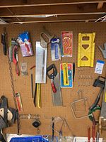 Pegboard mounted tools including saws, axe, wire brush, miter box, safety goggles, tape measure, wrenches, and hardware items