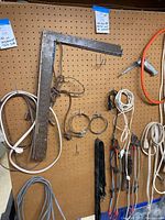 Pegboard view showing metal carpenter squares, several extension cords in white, orange, and gray, bungee cords with hooks, metal hose clamps, and a black leather tool belt.