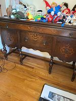 Full view of dark wood vintage buffet with inlaid decoration, brass pulls, standing on turned legs on hardwood floor, front view showing three drawers and two cabinets.