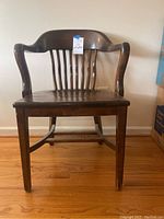 Full view of solid dark wood desk chair showing curved backrest with vertical slats and armrests, four straight legs, and worn wood finish.