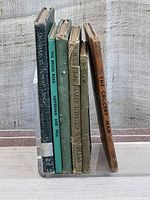 Six antique books standing upright, spines facing front showing titles and wear.