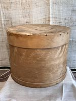 Front view of antique wooden round cheese box, showing intact lid and round shape with visible small missing wood on the edge of lid.
