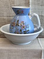 Front view of antique water pitcher with floral design set inside white bowl