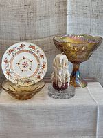 Four items displayed including carnival glass compote, amber glass bowl, carved candle on cut glass holder, and Royal Worcester plate