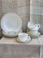 Stack of 4 cups, 4 saucers, and 4 shallow bowls with gold trim edges, all translucent white milk glass.