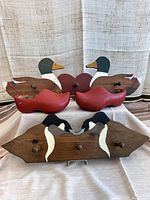 Front view of two wooden duck wall hangers and a pair of antique wooden shoes on a cloth background.