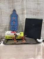 Wide view showing all the items on a silver plated tray including the log book, two donkey head openers, two books, painted candle holder and a ceramic bird on tray.