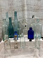 Lot of 16 antique and vintage glass bottles on display. Various sizes, shapes, and colors ranging from clear to blue tint. Showcases embossed Philips Bros Victoria BC bottle prominently.