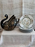 Full view showing 6 Mikasa Kabuki side plates stacked and one plate displayed, alongside black ceramic swan vase with gold highlights.