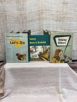 Three vintage children's books: Let's Go (Science and Conservation), Sammy Moves to Brookdale, Helping Others. All show wear and age.