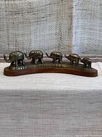 Front view of the statuette showing the five brass elephants arranged in descending size on curved wooden base.