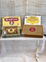 Four vintage cardboard cigar boxes sitting upright showing front labels and design variety