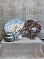 Photo showing all four items from lot: a Limoge floral tray, Royal Winton floral side plate, ceramic creamer, and round dresser top music box.