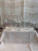 Full display of 8 Pyrex apothecary bottles and 1 measuring cup on a linen cloth surface.