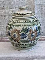 Front view showing bulbous pottery container with floral painted design and matching lid