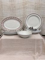 Group photo showing 4 platters, 4 soup bowls, 2 cereal bowls all with brown decorative rims and a white base, and metal duck sculpture.