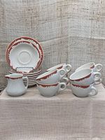 Complete set of 8 cups stacked on 8 saucers with 1 side plate and 1 creamer in front, showing pink leaf design on white ceramic.