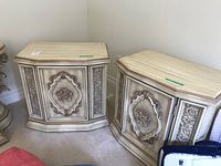 Pair of wood side tables in cream with gilded carved floral and scroll details on front paneling.