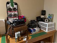 Wide view of lot showing leather case with Pentax SLR, filter pouch, telephoto lens, multiple cameras in a white basket, memory card and Kodak Brownie