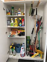 Cabinet with cleaning products on shelves and cleaning tools hanging and standing inside.