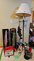 Overall view of floor lamp, canvas bag, boxed lures, decorative items, hats, coaster and book arranged on floor