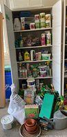 Full view of garden supply cabinet filled with various containers of plant nutrients, fertilizers, sprays, gloves, pots, and a watering can.
