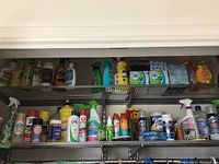 Various cleaning product bottles and tissue packs arranged on metal shelving, includes sprays, wipes and bottles from multiple brands.