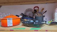 Shelf with cookware and utensils including frying pans and wooden spoons behind the pot