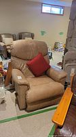 Front view of tan leather recliner with red accent pillow in upright position
