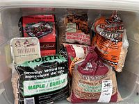 Full view of several partial bags and one foil container of various wood chips for smoking and BBQ including French Oak, Maple, Mesquite, and Hickory.