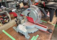 Full view of miter saw on table showing blade, base, handle and sliding rails
