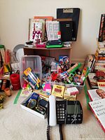 Wide view of office supplies lot including bins with assorted sticky notes, notebooks, writing tools, and a Bell phone on carpet.