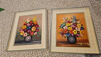 Two framed colorful flower bouquet still life oil paintings by Lordea on carpeted floor.