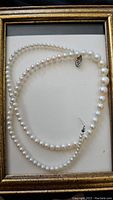 Full view of the pearl necklace elegantly displayed on a light background inside a frame, showing the full length of the pearls and clasp.