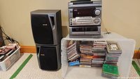Full view of Aiwa stereo system, speakers stacked, and tote full of assorted CDs