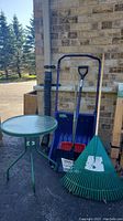 Full view of patio table with yard tools including shovels and rakes against brick wall.