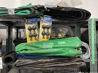 Side view of stacked tarps in various colors with two packs of 4 tarp grabbers on top and brass eyelets visible in a plastic bag